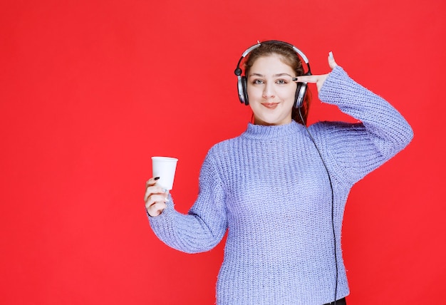 Mädchen mit Kopfhörern, die eine Kaffeetasse halten und denken.