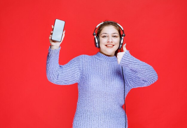 Mädchen mit Kopfhörern, die ihr Smartphone demonstrieren und sich glücklich fühlen.