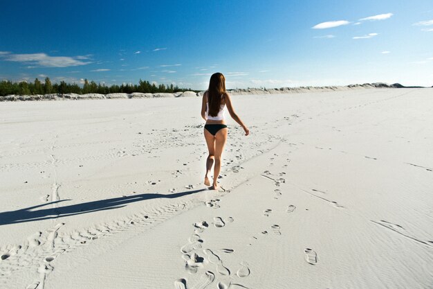 Mädchen mit langen Haaren geht auf den weißen Strand