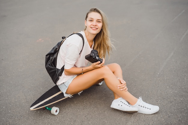 Mädchen mit langen Haaren mit Skateboard fotografieren vor der Kamera. Straße, aktiver Sport