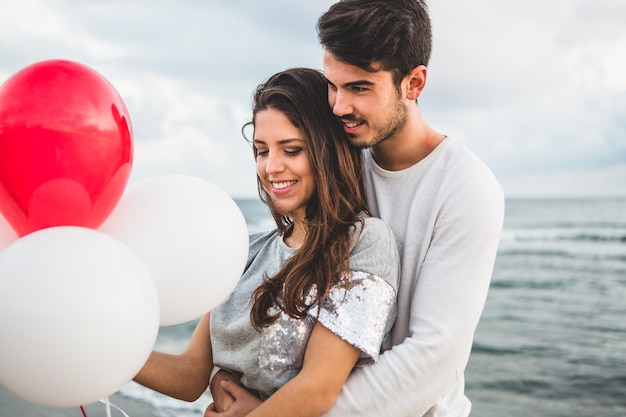 Mädchen mit Luftballons, während ihr Freund umarmt sie mit dem Meer Hintergrund