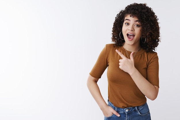 Mädchen mit offenem Mund wunderte sich und zeigte mit dem linken Zeigefinger. Schau dir den tollen Werbeverkauf an Augenbrauen heben glücklich begeistert