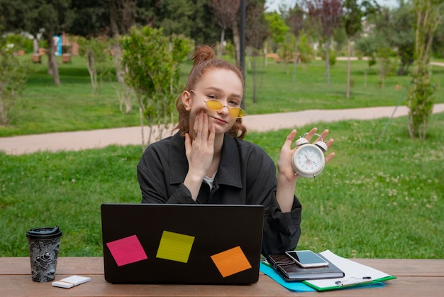 Mädchen mit roten Haaren, die im Park arbeiten und eine Uhr zeigen