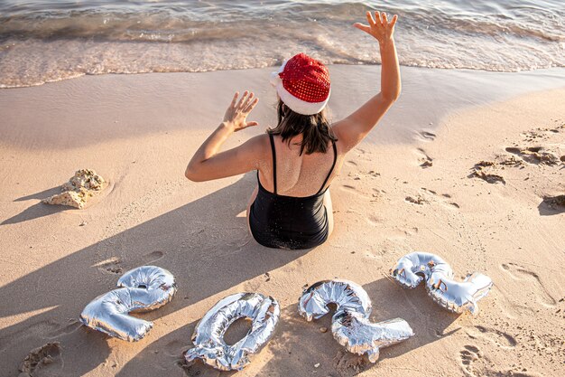 Mädchen mit silbernen Ballons in Form von Zahlen für das kommende Jahr am Meer