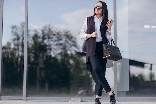 Mädchen mit Sonnenbrille mit einer Tasche auf einem dunklen Glas gelehnt