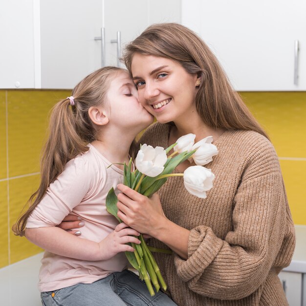 Mädchen mit Tulpen küssen Mutter auf Backe