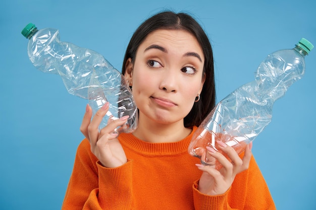 Kostenloses Foto mädchen mit zwei plastikflaschen denkt nach und schaut beiseite und sortiert den müll, um den planeten durch recycling zu retten