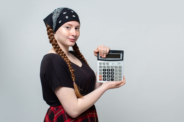 Mädchen schön mit Bandana rotem Rock und schwarzem T-Shirt, das Taschenrechner auf grau hält