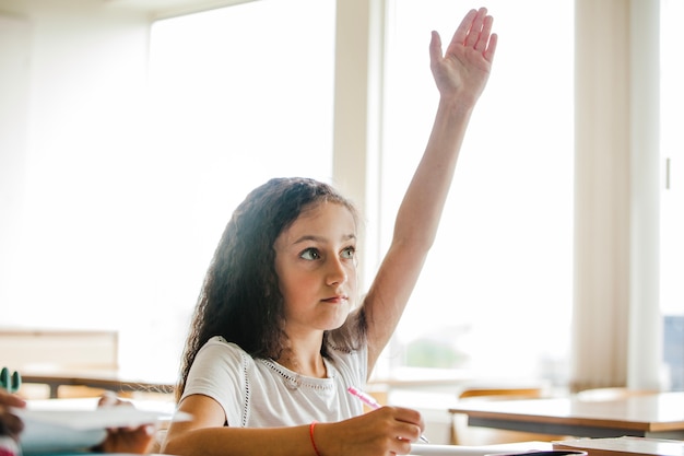 Mädchen sitzt am Schultisch heben Hand