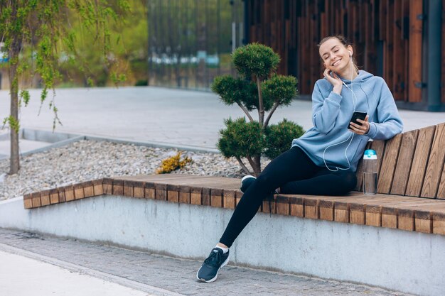 Mädchen sitzt auf dem Bein auf der Bank und hört Musik