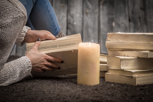 Kostenloses Foto mädchen sitzt auf dem boden, umgeben von vielen weißen büchern und einer großen kerze