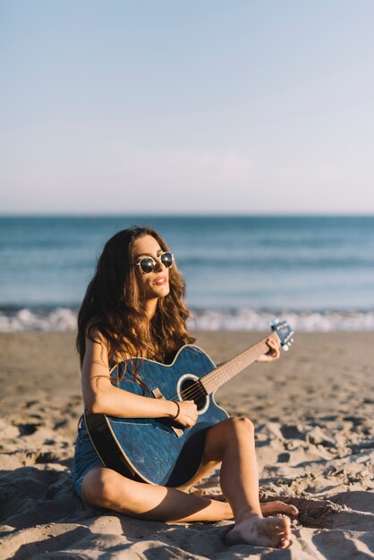 Mädchen spielt die Gitarre am Strand sitzen