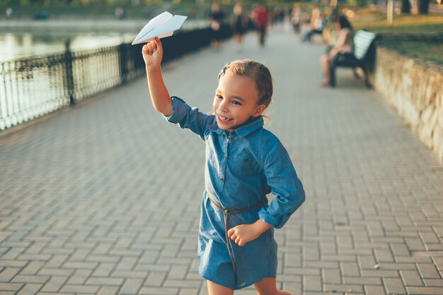 Mädchen spielt, läuft mit Spielzeugpapierflugzeug