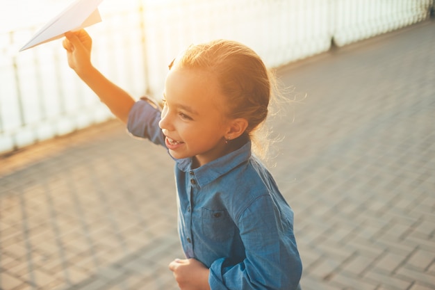 Mädchen spielt, läuft mit Spielzeugpapierflugzeug