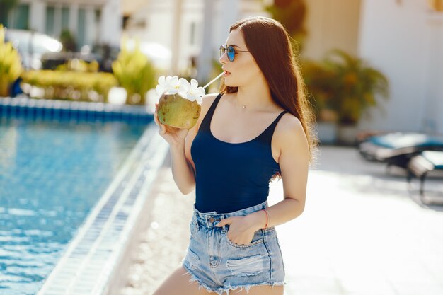 Mädchen trinkt frischen Saft aus einer Kokosnuss am Pool