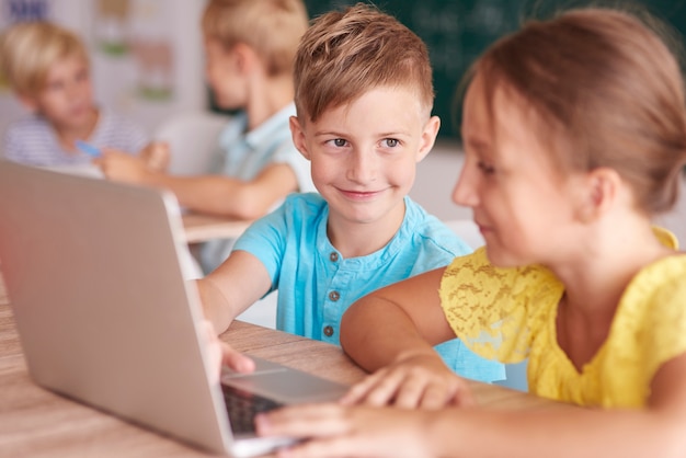 Mädchen und Junge, die den Computer im Klassenzimmer benutzen