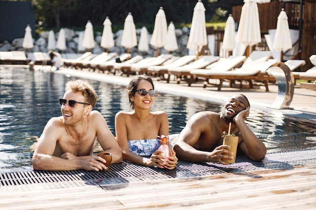 Mädchen und zwei ihre männlichen Freunde, die nahe Swimmingpool sich entspannen. Mädchen mit weißer und blauer Badebekleidung