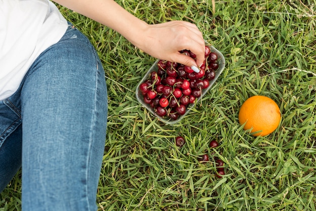 Mädchen, welches die Kirschen sitzen auf dem Gras nimmt