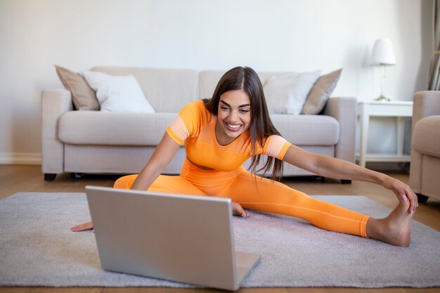 Mädchentraining zu Hause beim Training und Ansehen von Videos auf Laptop-Training im Wohnzimmer Schöne Frau streckt ihre Beine aus Sie sieht sich Videos im Internet an und wiederholt die Aufgaben