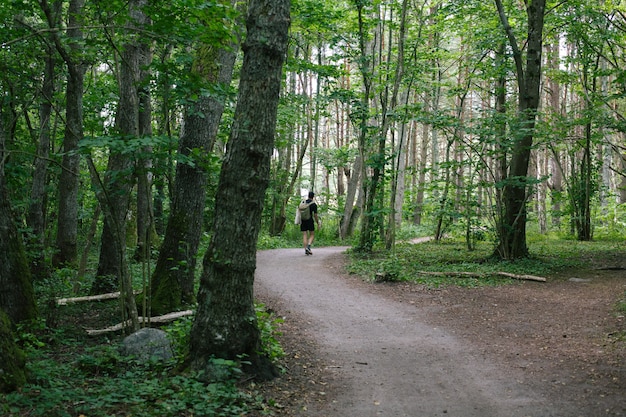 Männchen mit einem Rucksack, der auf einem Weg in der Mitte des Waldes geht