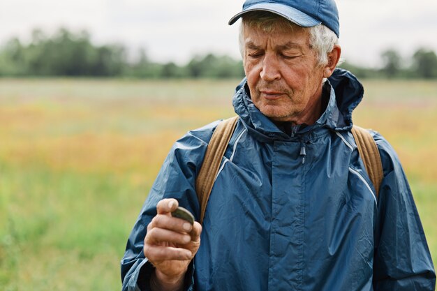 Männchen mittleren Alters mit blauer Jacke, die alte Münze auf der Wiese hält,