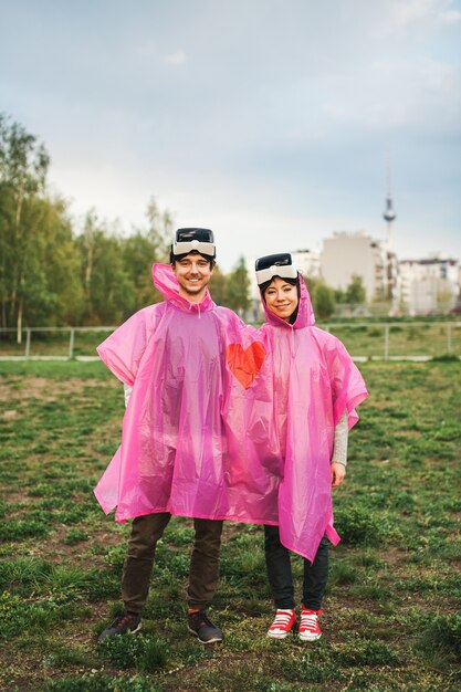 Männchen und Weibchen stehen auf dem Feld in einem gemeinsamen rosa Plastikregenmantel und nehmen VR-Headsets ab