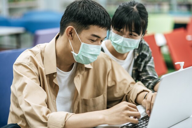 Männer und Frauen tragen Masken und suchen mit einem Laptop in der Bibliothek nach Büchern.