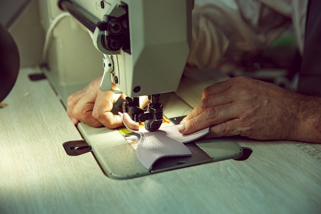 Männerhände hinter dem Nähen. Lederwerkstatt. Textil Vintage Industrie. Der Mann im Frauenberuf. Konzept der Gleichstellung der Geschlechter