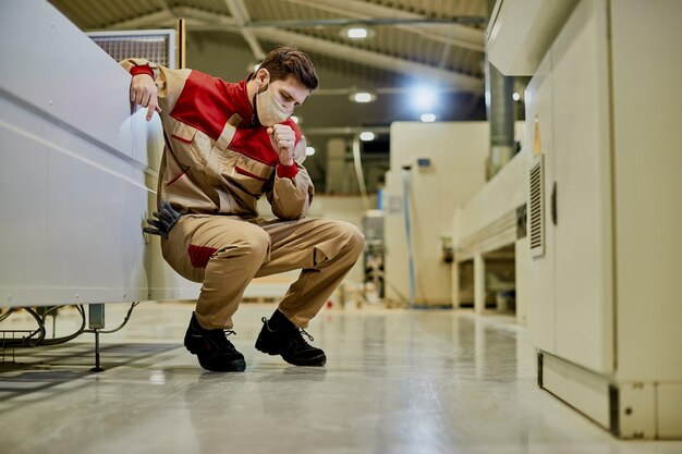 Männliche Arbeiter fühlen sich unwohl und husten, während sie während der Coronavirus-Pandemie in der Fabrik arbeiten