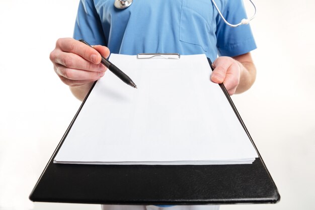 Männliche Doktorhand, die einen Stift und ein Klemmbrett mit leerem Papier und Stethoskop lokalisiert auf weißer Wand hält