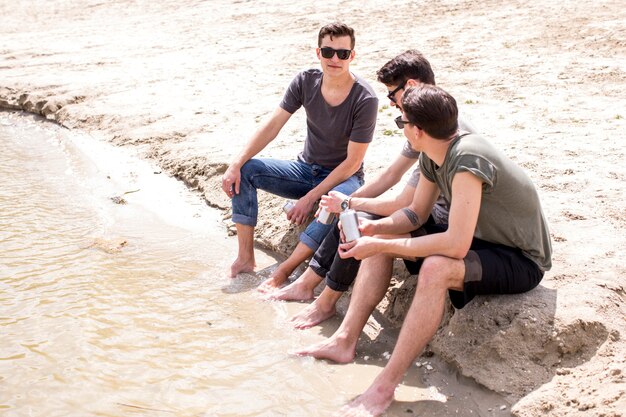 Männliche Freunde, die Sommer beim Sitzen auf Strand genießen