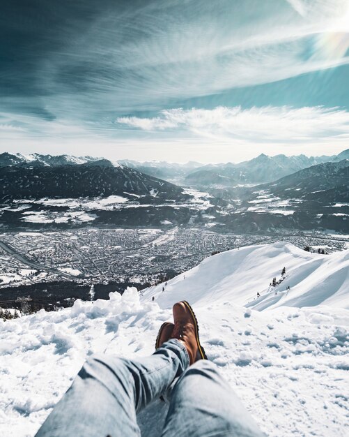 Männliche Füße sitzen auf einer schneebedeckten Klippe unter dem schönen bewölkten Himmel