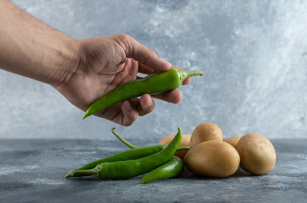 Männliche Hände, die grüne Chilischoten auf Marmorhintergrund halten