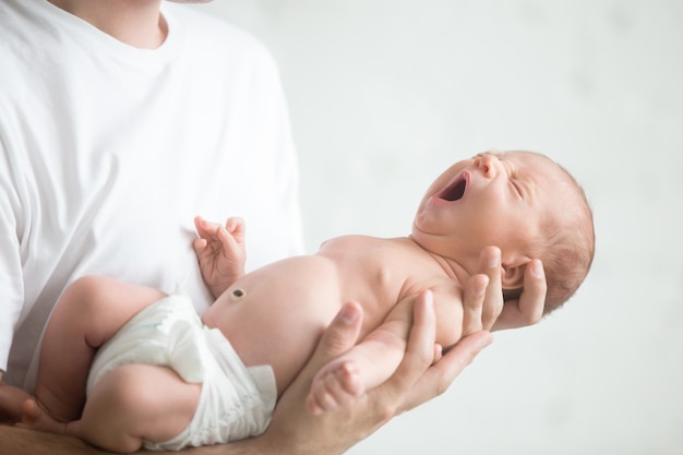 Männliche Hände halten ein schreiender Neugeborener