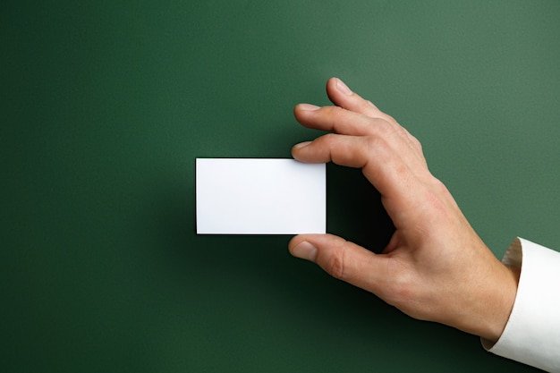 Männliche Hand, die eine leere Visitenkarte auf grüner Wand für Text oder Entwurf hält. Leere Kreditkartenvorlagen für den Kontakt oder die Verwendung in Unternehmen. Finanzamt. Copyspace.