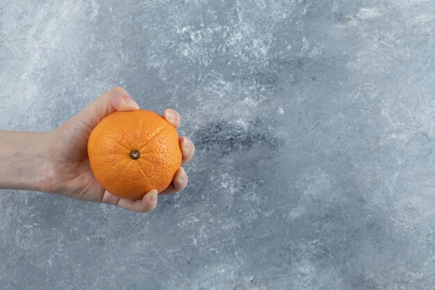 Männliche Hand, die einzelne Orange auf Marmortisch hält.