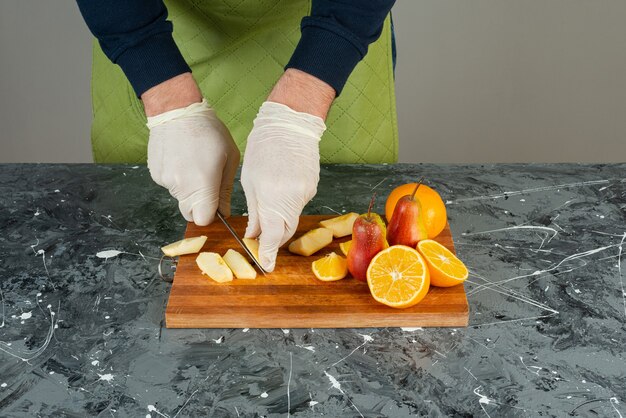 Männliche Hand, die frische rote Äpfel auf Marmortisch schneidet.