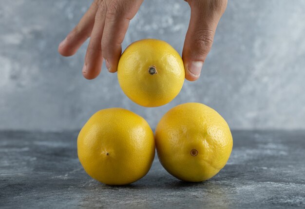 Männliche Hand, die frische Zitrone vom Stapel nimmt.