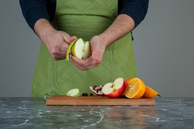 Männliche Hand, die frischen Apfel oben auf Holzbrett auf Tisch schält.