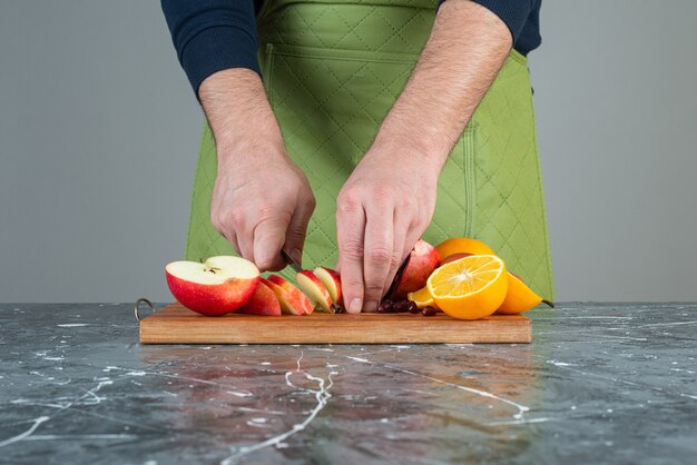 Männliche Hand, die frischen Apfel oben auf Holzbrett auf Tisch schneidet.