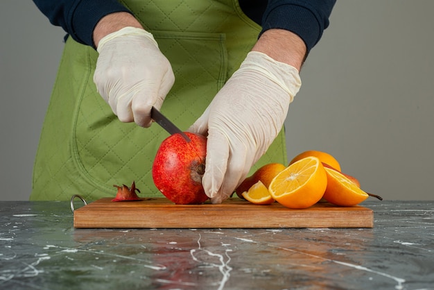 Männliche Hand, die frischen Granatapfel auf Holzbrett auf Tisch schneidet.