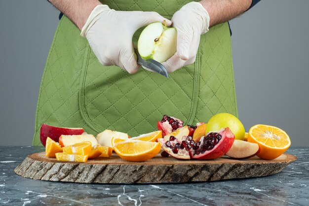 Männliche Hand, die grünen Apfel oben auf Holzbrett auf Tisch schneidet.