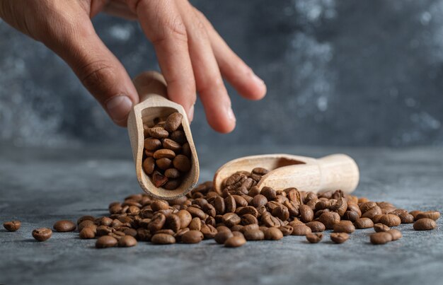 Männliche Hand, die hölzernen Löffel aromatischer Kaffeebohnen auf Marmorhintergrund hält