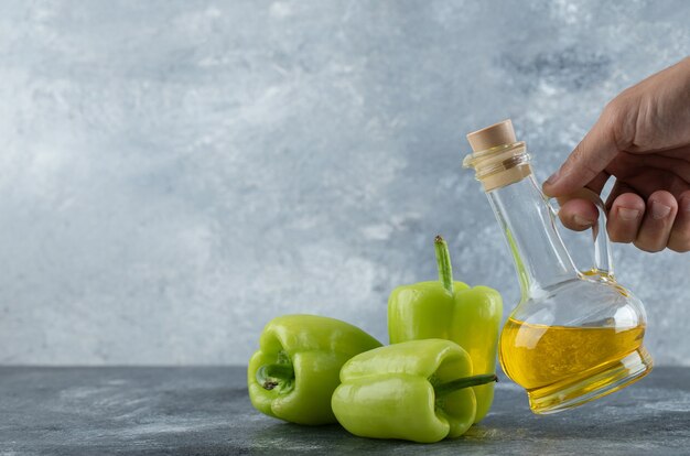 Männliche Hand, die Ölflasche vom Tisch und frische Paprika auf dem Tisch nimmt.