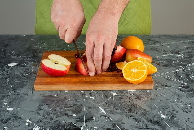 Männliche Hand, die roten Apfel auf Holzbrett auf Tisch schneidet.