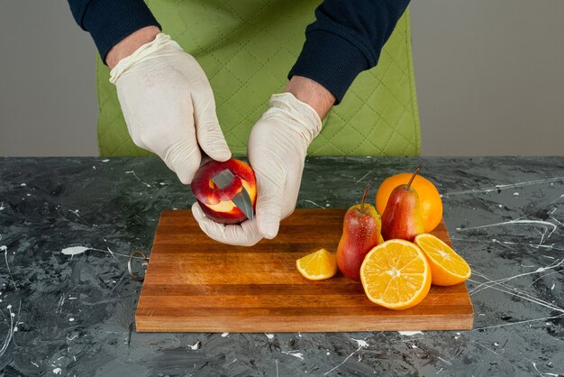 Männliche Hand, die roten Apfel oben auf Holzbrett auf Tisch schält.