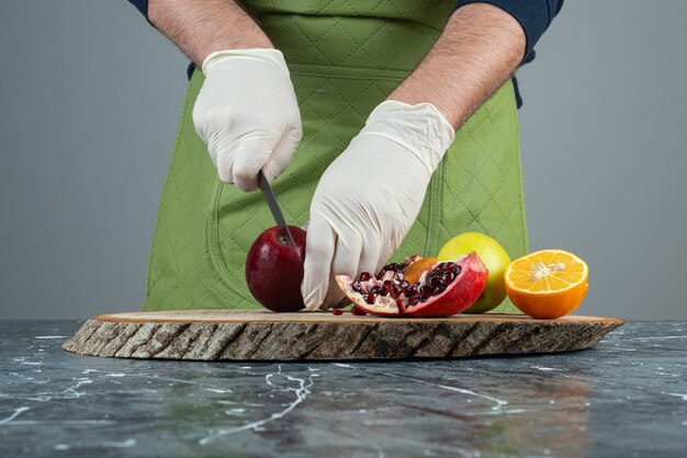 Männliche Hand, die roten Apfel oben auf Holzbrett auf Tisch schneidet.