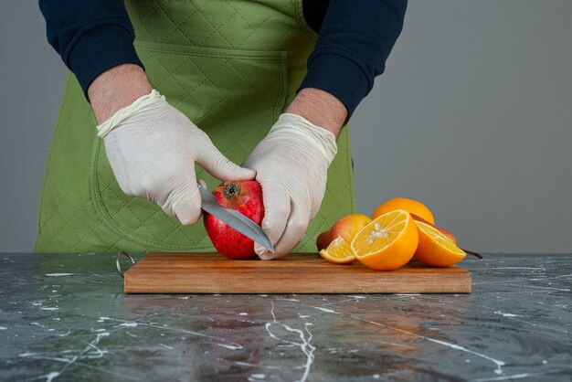 Kostenloses Foto männliche hand, die roten apfel oben auf holzbrett auf tisch schneidet.