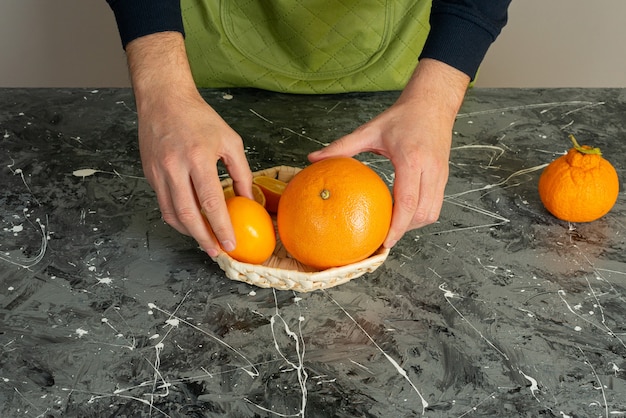 Männliche Hand, die saftige orange Früchte auf Marmortisch hält.