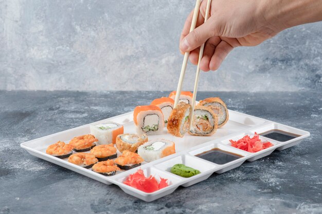 Männliche Hand, die Sushi-Rolle mit Stäbchen vom weißen Teller nimmt